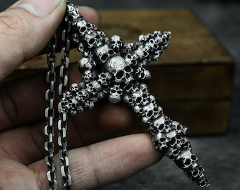 May include: A silver pendant necklace featuring a cross made of dozens of tiny skulls. The chain is silver and has a box link design.