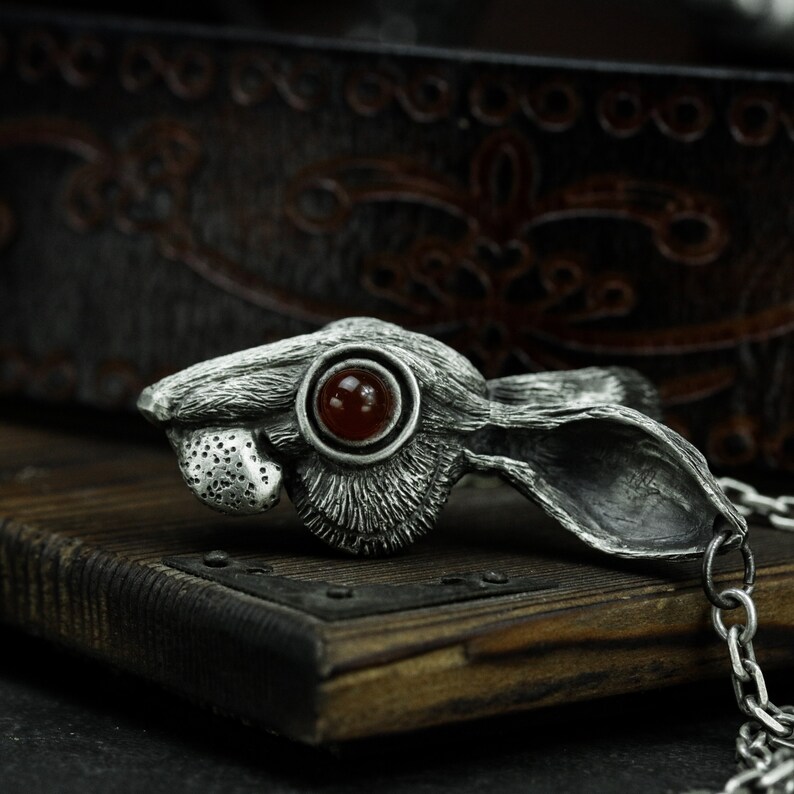 May include: A silver rabbit pendant with a red gemstone eye. The pendant is attached to a silver chain.