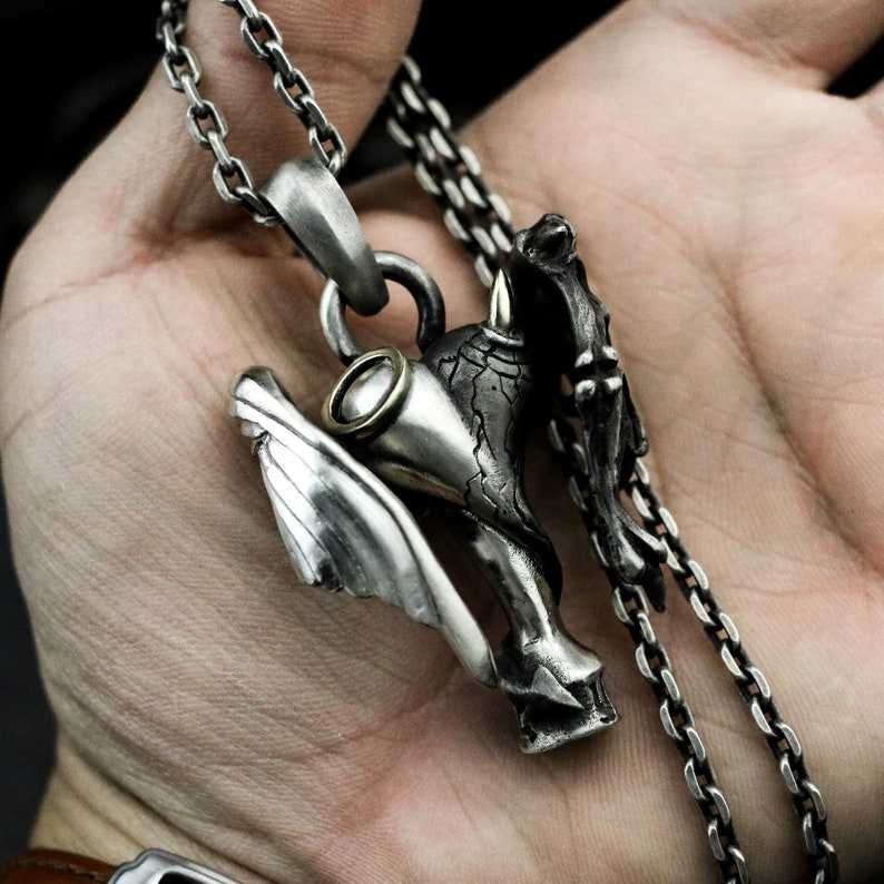 Puede incluir: Un collar con un colgante de plata que presenta un dise&ntilde;o tridimensional detallado de una criatura alada con un cuerno. El colgante est&aacute; unido a una cadena de plata.