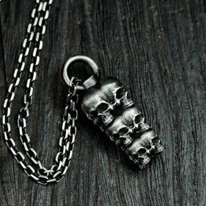 May include: A silver chain necklace with a pendant featuring a stack of five detailed skull sculptures.