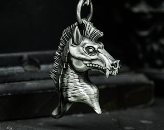 May include: A silver pendant necklace featuring a detailed, stylized, dragon-like creature head with a toothy grin.