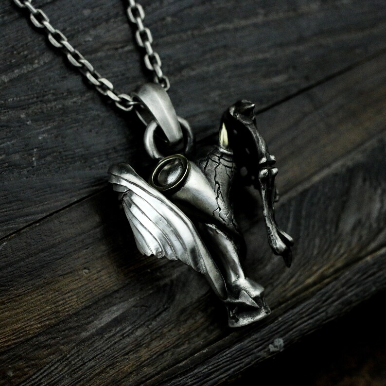 Puede incluir: Collar con colgante de plata que presenta una figura alada detallada con una espada y un ojo de piedra preciosa. El colgante est&aacute; unido a una cadena de plata.