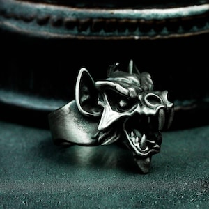 May include: A silver ring with a detailed, snarling gargoyle design. The ring is made of metal and has a textured finish.