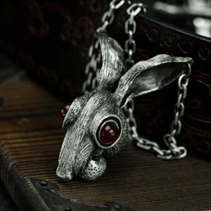 May include: A silver rabbit pendant with red gemstone eyes. The pendant is attached to a silver chain.