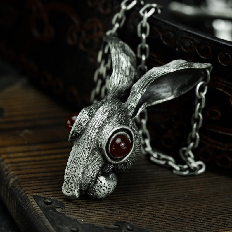 May include: A silver rabbit pendant with red gemstone eyes. The pendant is attached to a silver chain.