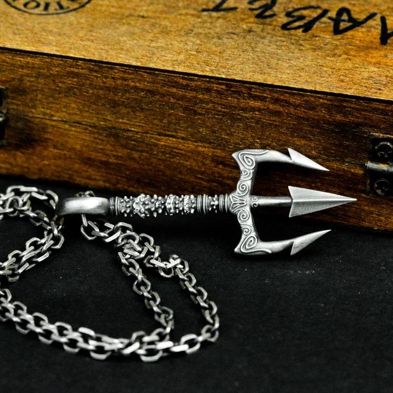 May include: A silver trident necklace with a detailed design and a silver chain. The trident is a popular symbol of power and strength.