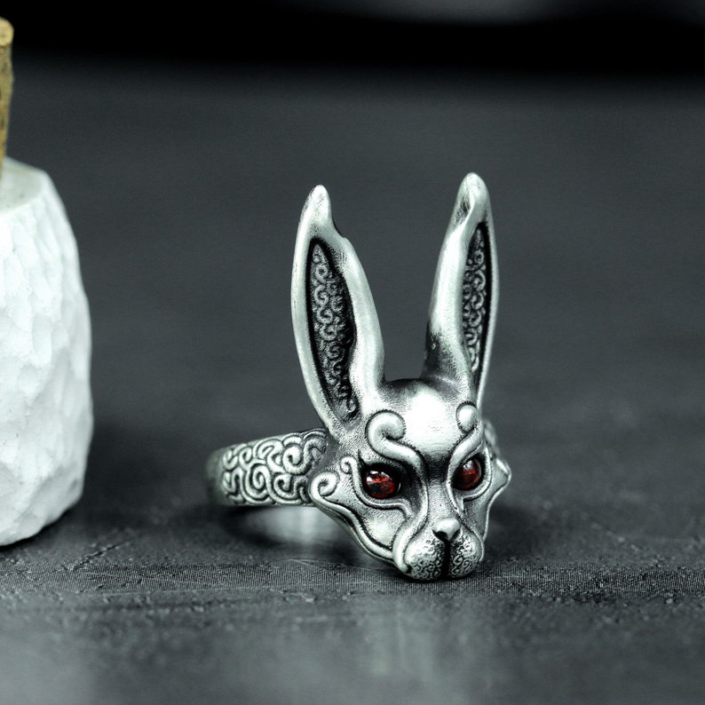 May include: A silver ring with a detailed rabbit head design. The rabbit has red eyes and intricate patterns on its ears and face.