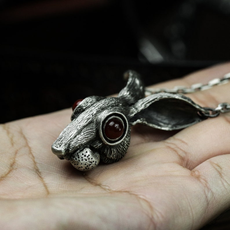 May include: A silver rabbit pendant necklace with red gemstone eyes. The rabbit's head is detailed with fur and whiskers.