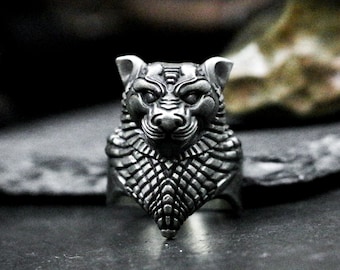 May include: A silver ring featuring a detailed wolf head design. The wolf's face is intricately sculpted with a textured, scaly pattern.