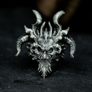 May include: A silver ring featuring a detailed dragon head design. The dragon has horns, sharp teeth, and a fierce expression.