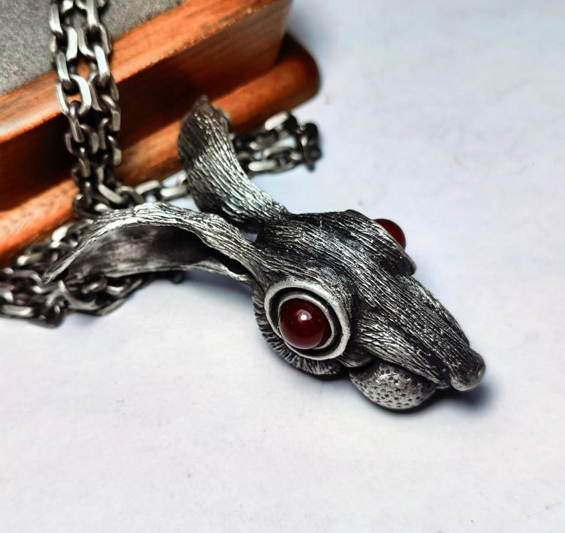May include: A silver pendant necklace featuring a detailed rabbit head with red gemstone eyes. The rabbit's fur is textured and the pendant is attached to a silver chain.