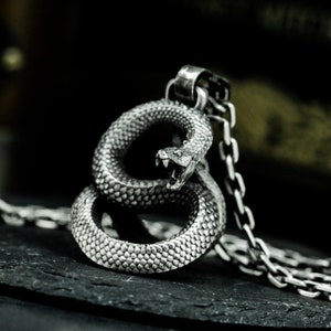 May include: A silver snake pendant necklace with a coiled snake design. The snake has a detailed textured surface and an open mouth.