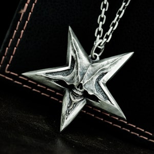May include: A silver star-shaped pendant with a skull face in the center. The pendant is attached to a silver chain.