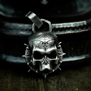May include: A silver skull pendant with intricate details and a spiked halo. The skull has a detailed face with a prominent nose and eye sockets.