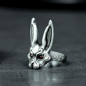 May include: A silver ring with a detailed rabbit head design. The rabbit has long ears and red eyes. The ring band is also decorated with a swirling pattern.