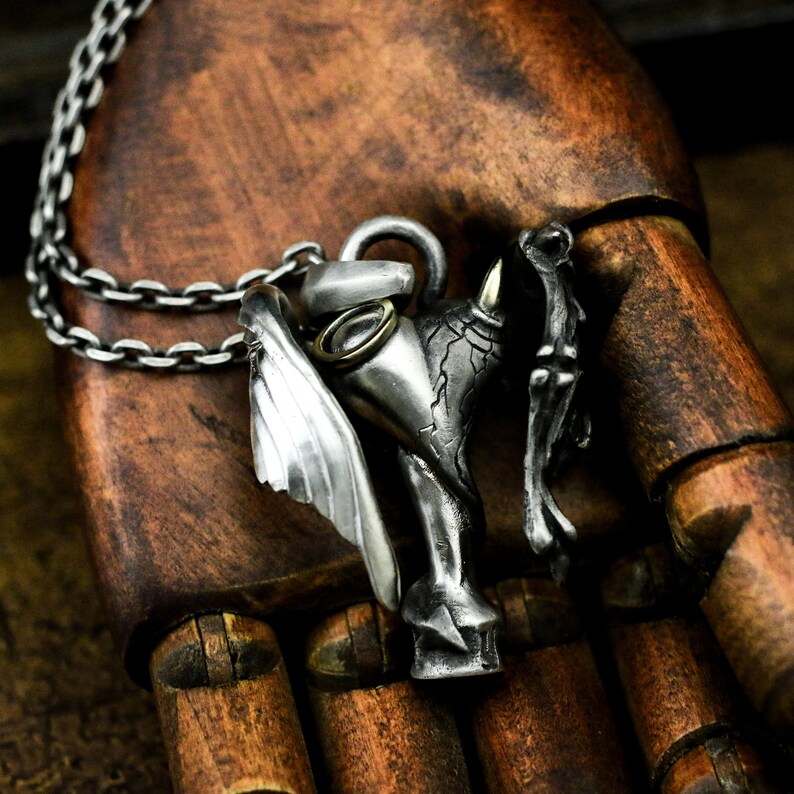 Puede incluir: Un collar con un colgante de plata que presenta una escultura detallada de una criatura alada con cabeza de toro. El colgante est&aacute; unido a una cadena de plata.