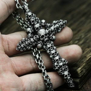 May include: A silver pendant necklace featuring a large cross made of dozens of tiny skull shapes. The chain is silver and has a box link design.