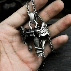 Puede incluir: Collar de cadena de plata con un colgante que representa una figura de demonio alado con una cabeza de calavera y una serpiente envuelta alrededor de su cuerpo. El colgante est&aacute; inscrito con las letras "KSD".