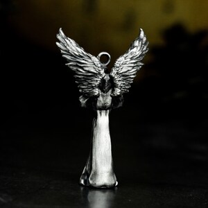 May include: A silver angel figurine with outstretched wings. The angel is wearing a long robe and has a halo.