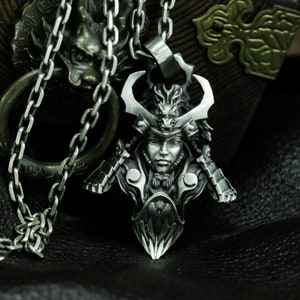 Puede incluir: Un collar con un colgante de plata que representa un busto detallado de un guerrero samur&aacute;i que lleva un casco con un dise&ntilde;o de drag&oacute;n. El colgante est&aacute; en una cadena de plata.