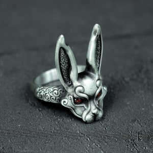 May include: A silver ring with a detailed rabbit head design. The rabbit has red eyes and intricate patterns on its fur.