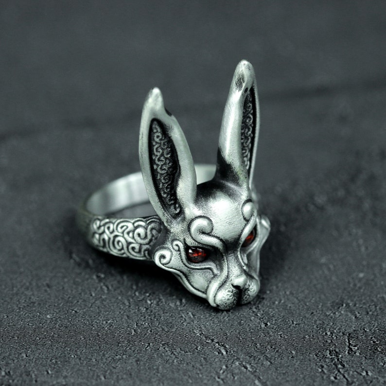 May include: A silver ring with a detailed rabbit head design. The rabbit has red eyes and intricate patterns on its fur.