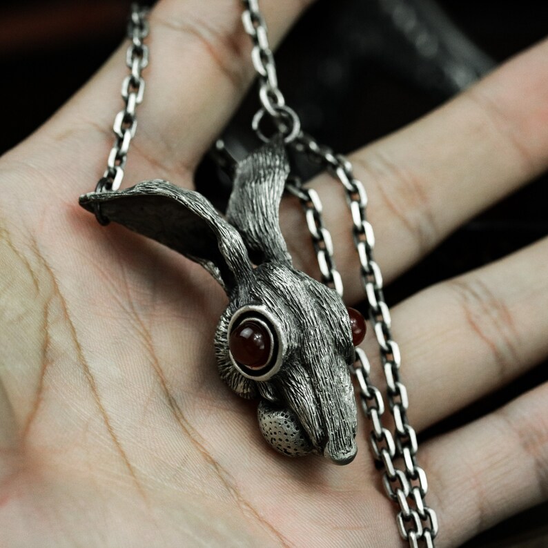 May include: A silver chain necklace with a detailed rabbit pendant featuring red gemstone eyes.