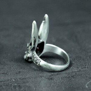 May include: A silver ring with a detailed rabbit design. The rabbit's ears are raised and the ring has a red gemstone in the center.