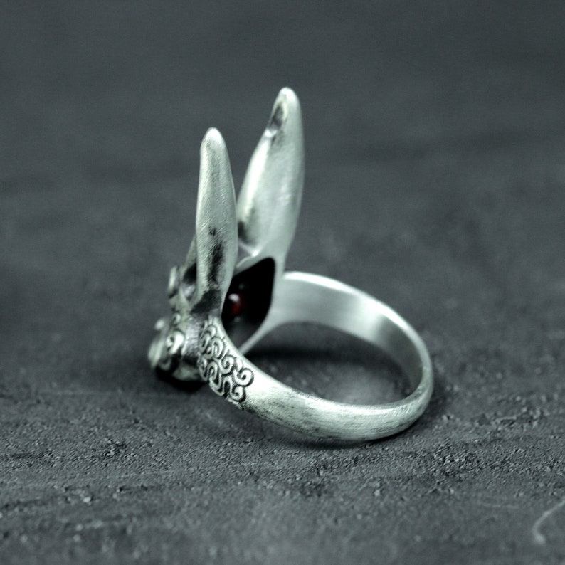 May include: A silver ring with a detailed rabbit design. The rabbit's ears are raised and the ring has a red gemstone in the center.