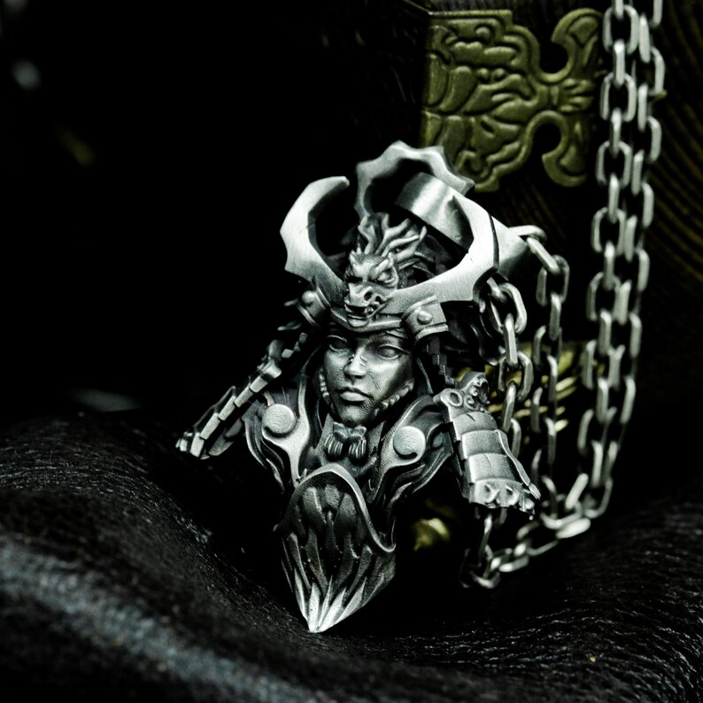 Puede incluir: Un colgante de plata que representa a un guerrero samur&aacute;i con un casco de drag&oacute;n. El colgante est&aacute; unido a una cadena de plata.