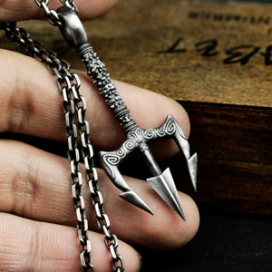 May include: A silver chain necklace with a detailed trident pendant. The trident has a textured design and a sharp point.