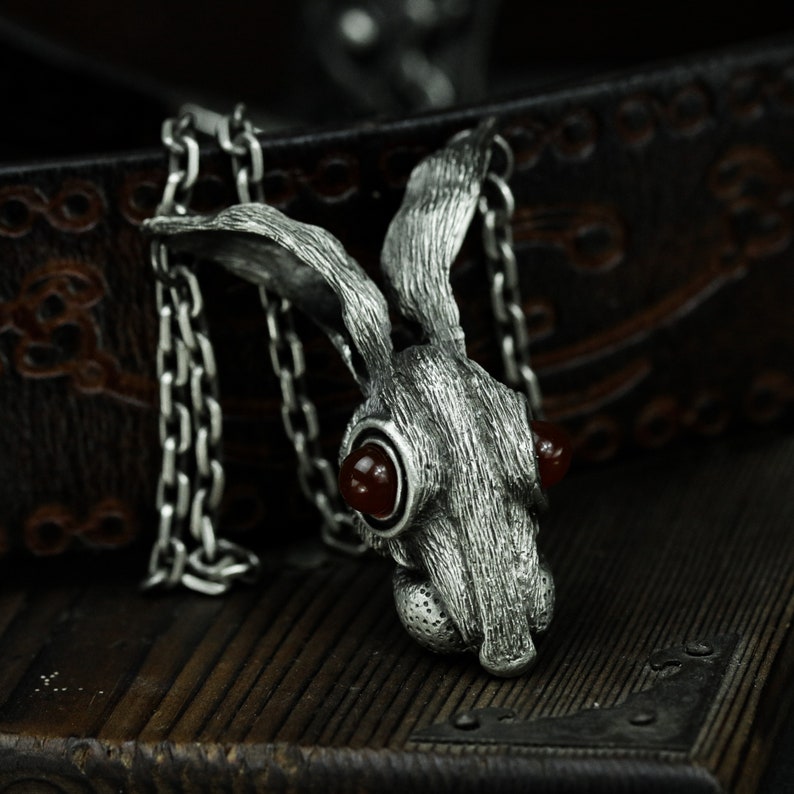 May include: A silver rabbit pendant necklace with red gemstone eyes. The pendant is detailed with textured fur and hangs from a silver chain.