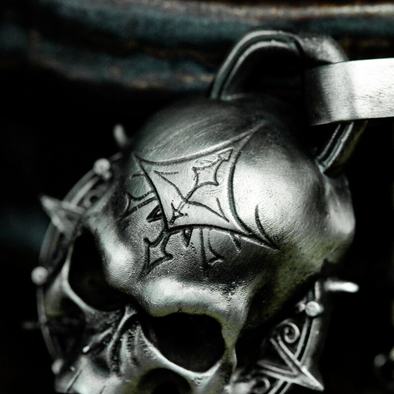 May include: A silver skull pendant with a detailed design and a spiked halo. The skull has a stylized cross etched on the forehead.