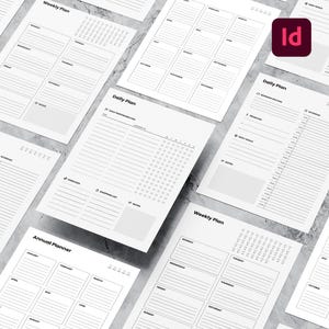 Peut inclure: Plusieurs pages de planificateur blanches avec du texte noir, dont "Weekly Plan", "Daily Plan" et "Annual Planner". Les pages sont disposées sur une surface gris clair. Un logo "Id" rouge et blanc est visible.