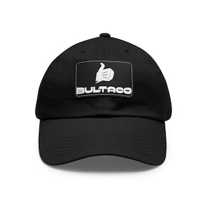 Può includere: Cappellino da baseball nero con una toppa bianca che mostra un gesto di pollice in su e la parola "BULTACO" in lettere bianche.