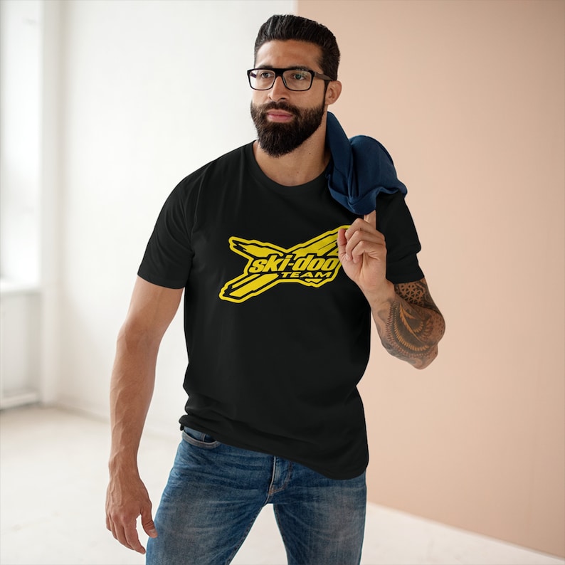 May include: A black t-shirt featuring a yellow Ski-Doo Team logo. The logo depicts a stylised ski with the words "Ski-Doo Team" in black text.