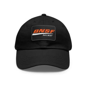 Op de afbeelding: Zwarte baseballcap met het BNSF Railway-logo. Het logo is een rechthoekige patch met de tekst "BNSF" in oranje en "RAILWAY" in wit, op een zwarte achtergrond. De cap heeft een gebogen klep en een verstelbare band.