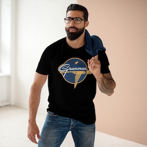 May include: A black t-shirt with a blue and gold logo that says "Grumman" with a star and a stylized eagle.