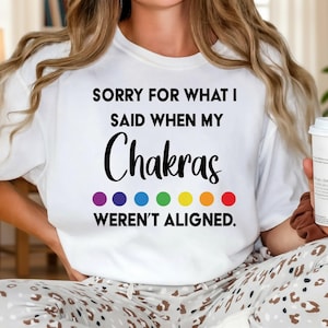 May include: White t-shirt with the text "SORRY FOR WHAT I SAID WHEN MY Chakras WEREN'T ALIGNED." The word "Chakras" is in a large, bold, black font. Below the word "Chakras" are seven colored circles in a rainbow pattern.