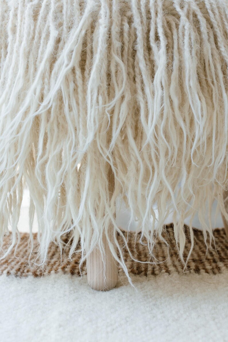 May include: A white fluffy stool with a wooden base. The stool is sitting on a brown and white rug.