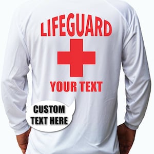 May include: White long-sleeve shirt with red text that says "LIFEGUARD" and a red cross. Below the cross is the text "YOUR TEXT". A white speech bubble with black text says "CUSTOM TEXT HERE".