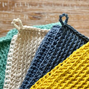 K&ouml;nnte beinhalten: Drei geh&auml;kelte Geschirrt&uuml;cher in verschiedenen Farben: Gelb, Blau und Gr&uuml;n. Die Geschirrt&uuml;cher sind &uuml;bereinander gestapelt, wobei das gelbe unten und das gr&uuml;ne oben liegt. Jedes Geschirrtuch hat einen Schlaufe.