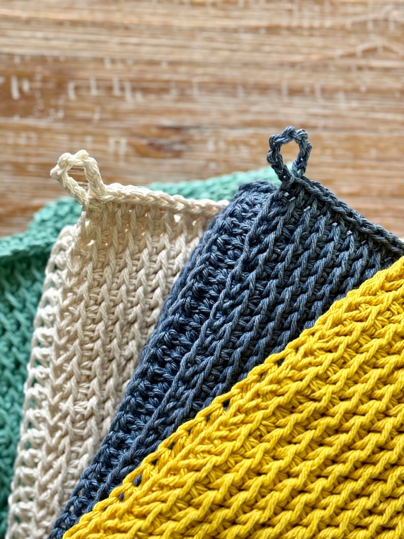 K&ouml;nnte beinhalten: Drei geh&auml;kelte Geschirrt&uuml;cher in verschiedenen Farben: Gelb, Blau und Gr&uuml;n. Die Geschirrt&uuml;cher sind &uuml;bereinander gestapelt, wobei das gelbe unten und das gr&uuml;ne oben liegt. Jedes Geschirrtuch hat einen Schlaufe.