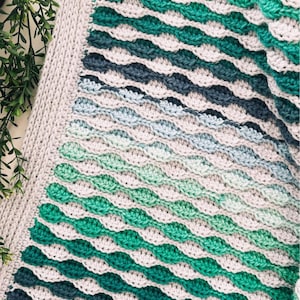 Może przedstawiać: Zestaw trzech ceramicznych kubków z nakrapianą, kremową glazurą. Każdy kubek ma inny ręcznie malowany wzór: niebiesko-zielony liść, żółty kwiat i czerwona jagoda. Kubki mają prosty, zaokrąglony kształt.