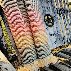 Pu&ograve; includere: Una coperta di uncinetto color arcobaleno con frange che pendono dal bordo. La coperta &egrave; drappeggiata su una panca di legno con una stella di metallo sul retro.