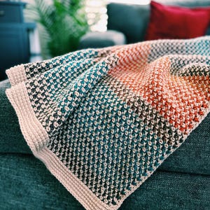Könnte beinhalten: Eine farbenfrohe, strukturierte Decke mit einem gewebten Muster. Die Decke hat einen Farbverlauf aus Farben, darunter Türkis, Orange und Creme. Die Kanten sind mit einem cremefarbenen Rand versehen. Diese gemütliche Decke ist perfekt für die Inneneinrichtung.