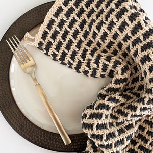 May include: A black and beige striped knitted dishcloth or tea towel on a brown plate with a gold fork.