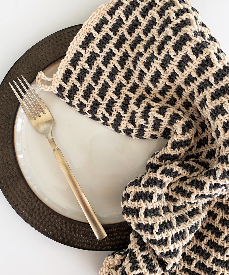 May include: A black and beige striped knitted dishcloth or tea towel on a brown plate with a gold fork.