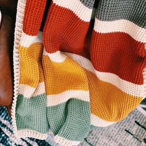 May include: A striped crocheted throw blanket in shades of gray, red, yellow, and green. The blanket has a white crocheted border.