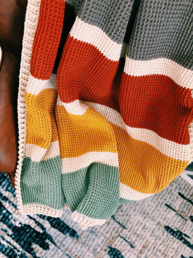 May include: A striped crocheted throw blanket in shades of gray, red, yellow, and green. The blanket has a white crocheted border.